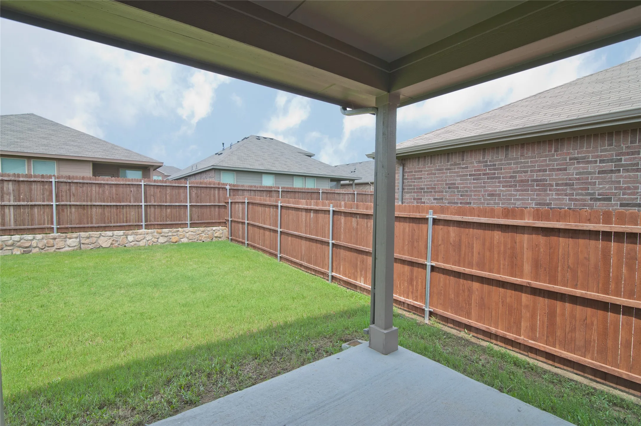 Covered patio with concrete flooring, private wood fencing, and a stone retaining wall