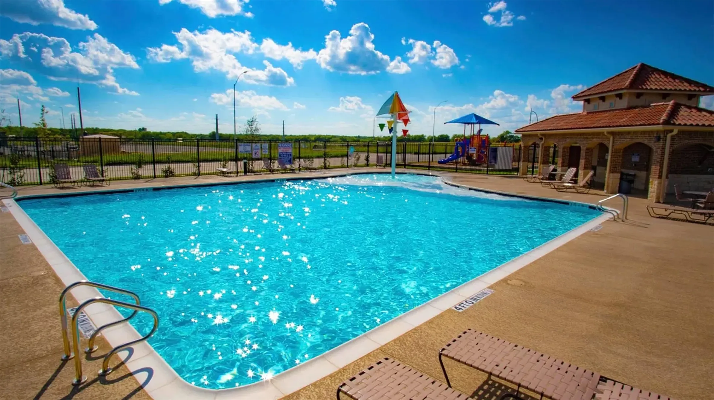 Community swimming pool with a dedicated splash pad, adjacent recreational building, and nearby playground structure