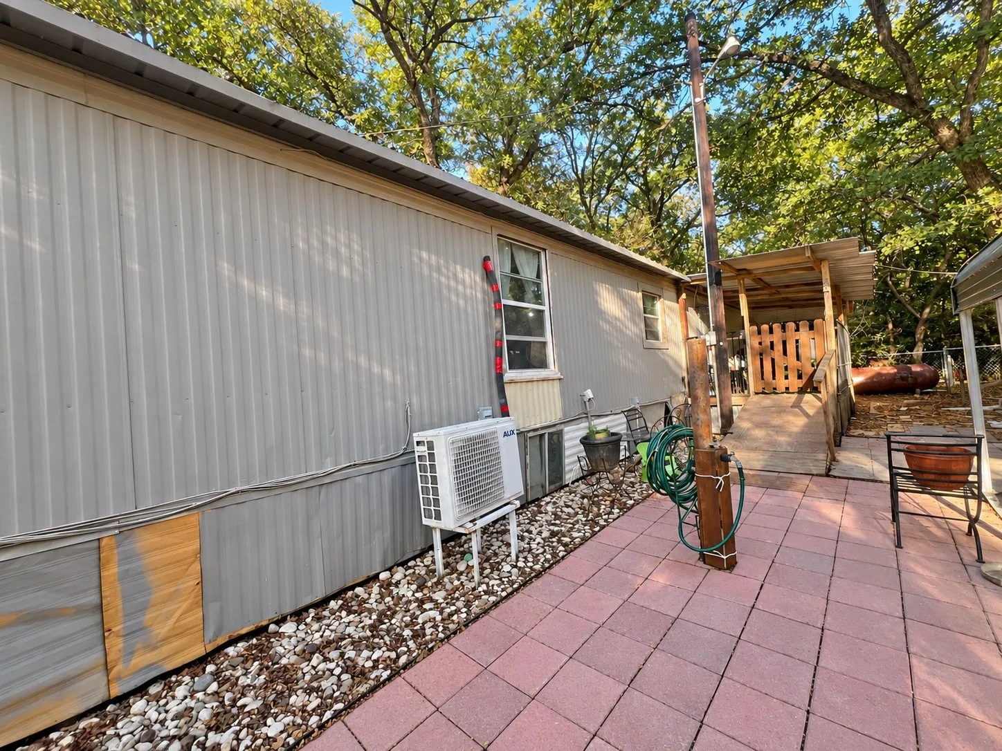 Patio area with red paver flooring, shaded porch with wooden fencing, and gravel landscaping