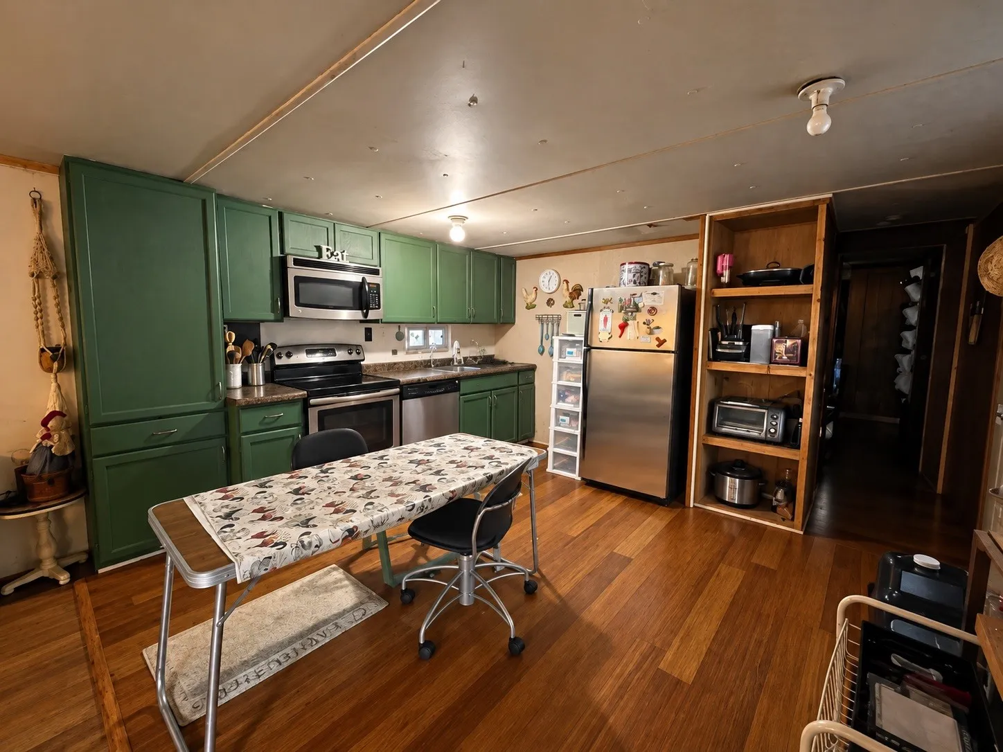 Kitchen featuring green cabinetry, stainless steel appliances, wood-finish flooring, and built-in shelving
