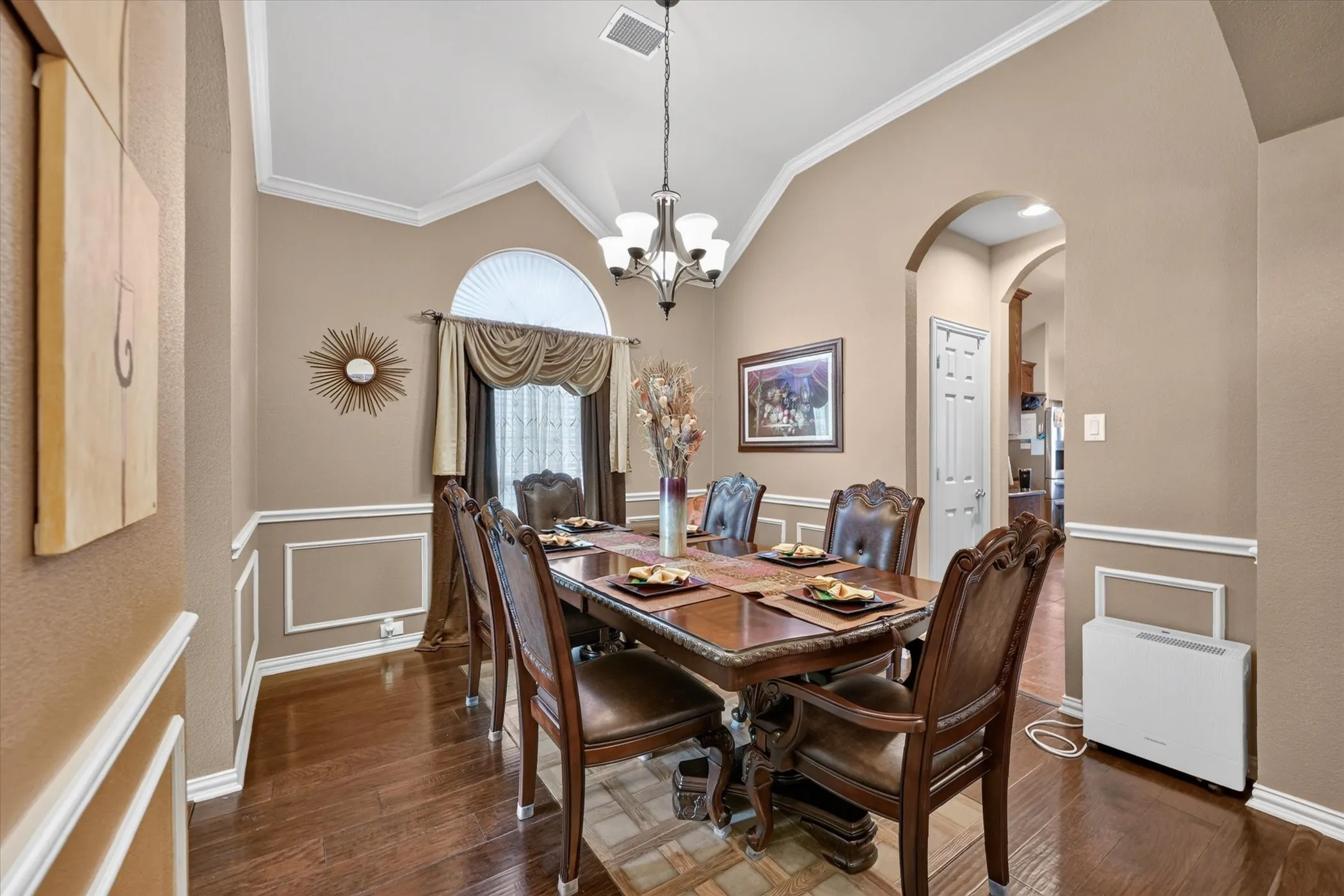Wood-finish flooring, vaulted ceiling, crown molding, arched entryways, and picture frame wainscoting