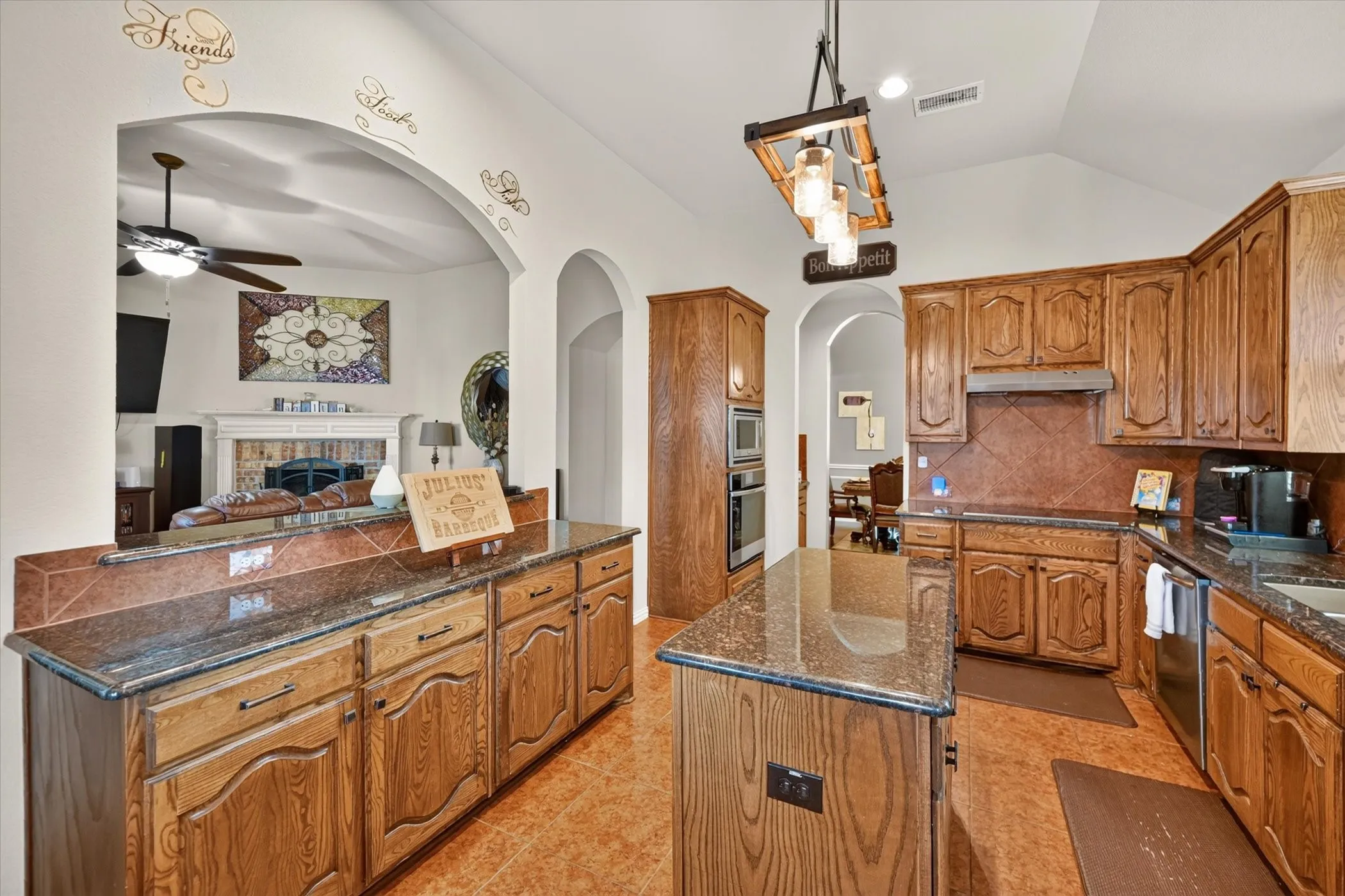 Kitchen featuring wood-finish cabinetry, granite countertops, tile flooring, an integrated double oven, and a central island
