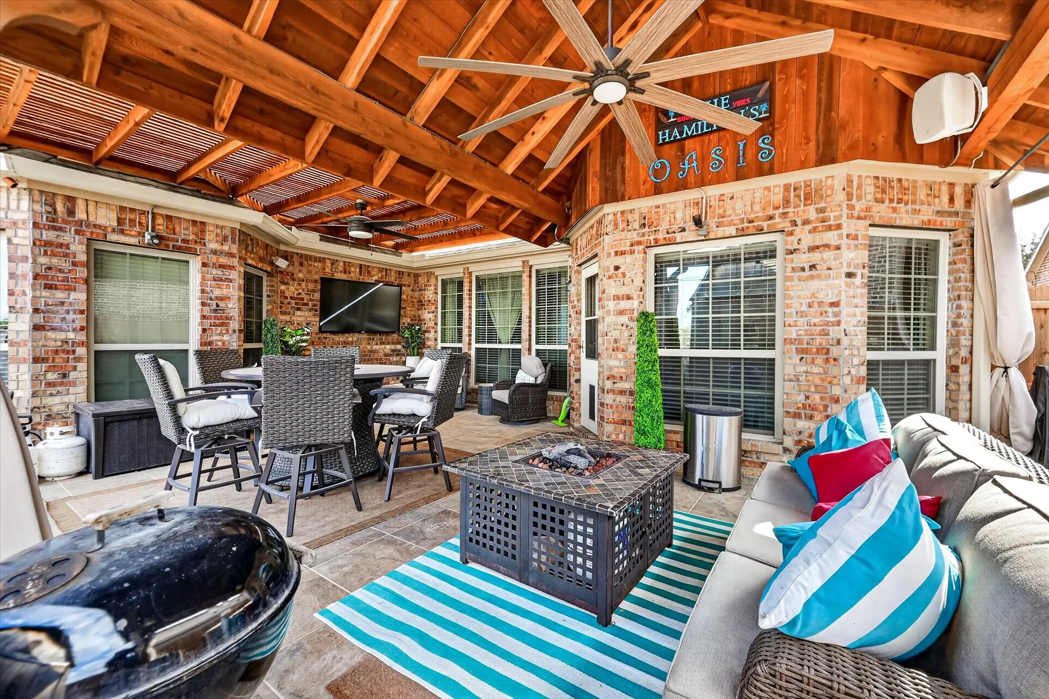 Covered outdoor patio featuring a wood-beamed ceiling, brick exterior, ceiling fans, and tiled flooring
