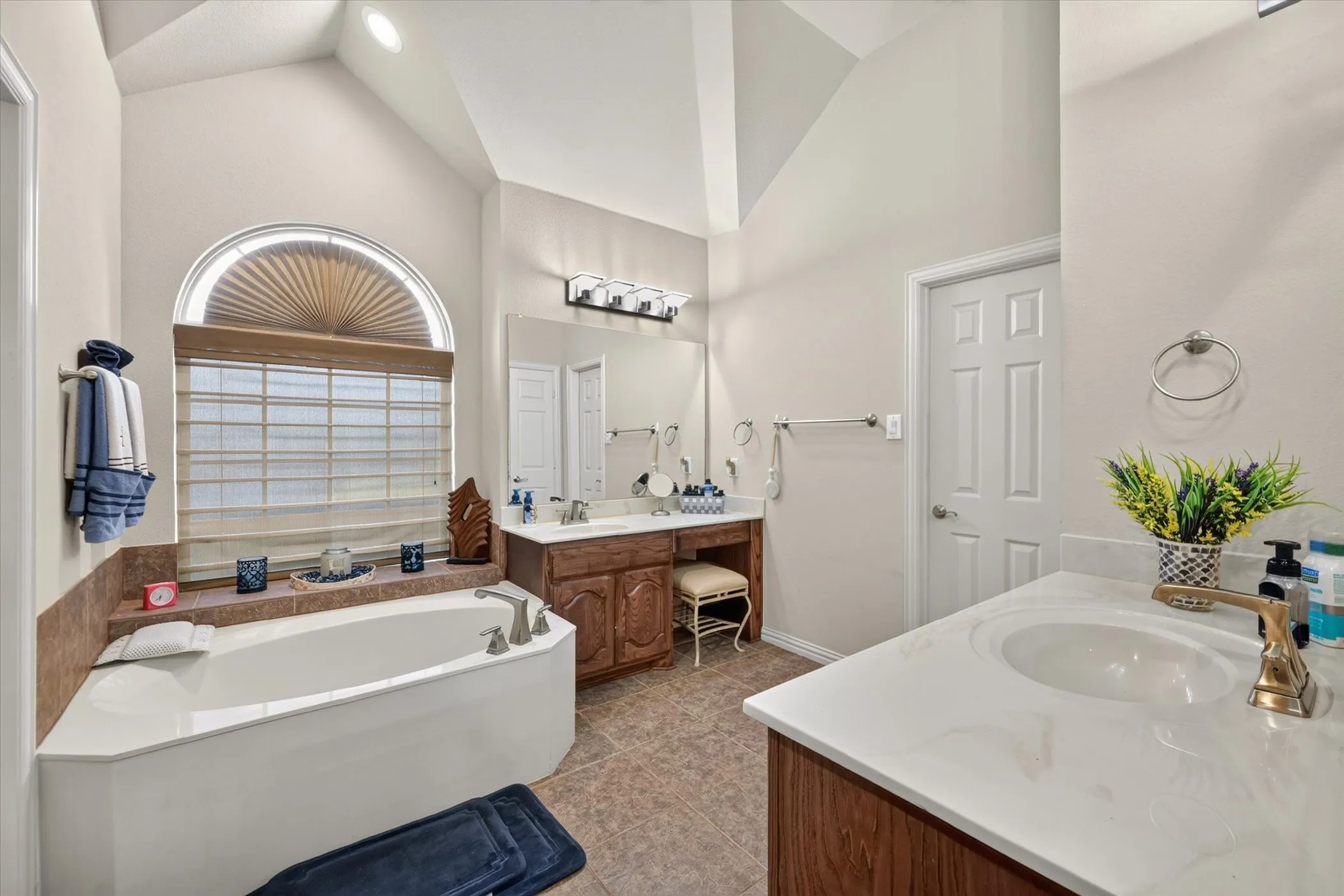 Soaking tub with tiled surround, arched window, and custom blinds