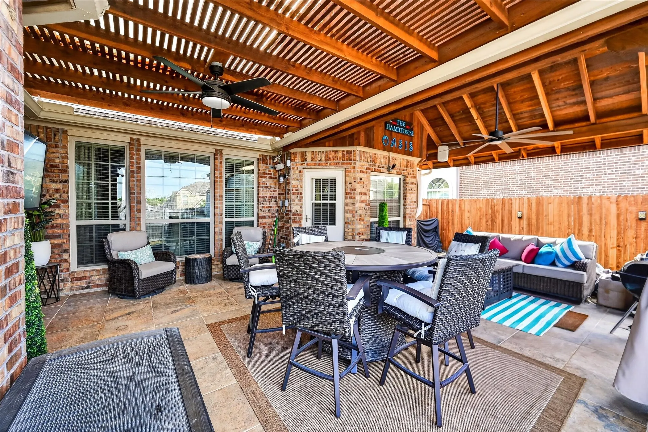 Expansive covered patio featuring a wood-slat ceiling, dual ceiling fans, brick exterior, and a privacy fence