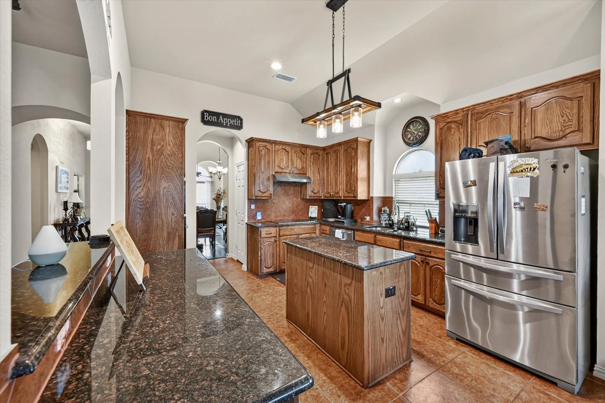 Kitchen featuring wood cabinetry, stainless steel appliances, a center island, and dark speckled countertops