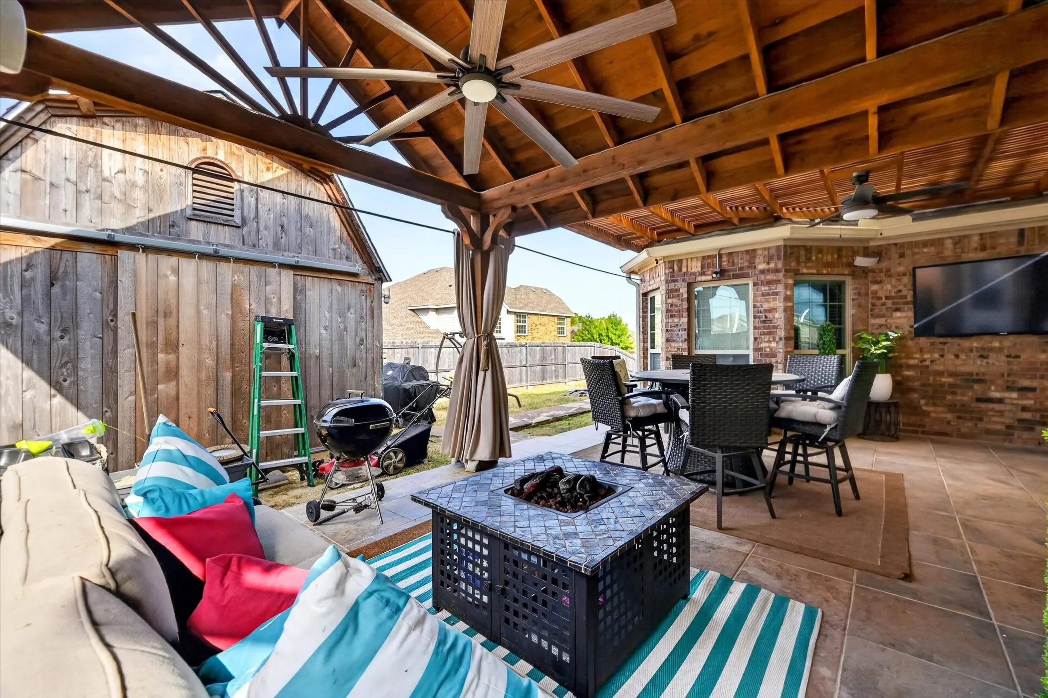 Covered patio with exposed wood beam ceiling, ceiling fans, tile flooring, and a brick exterior wall