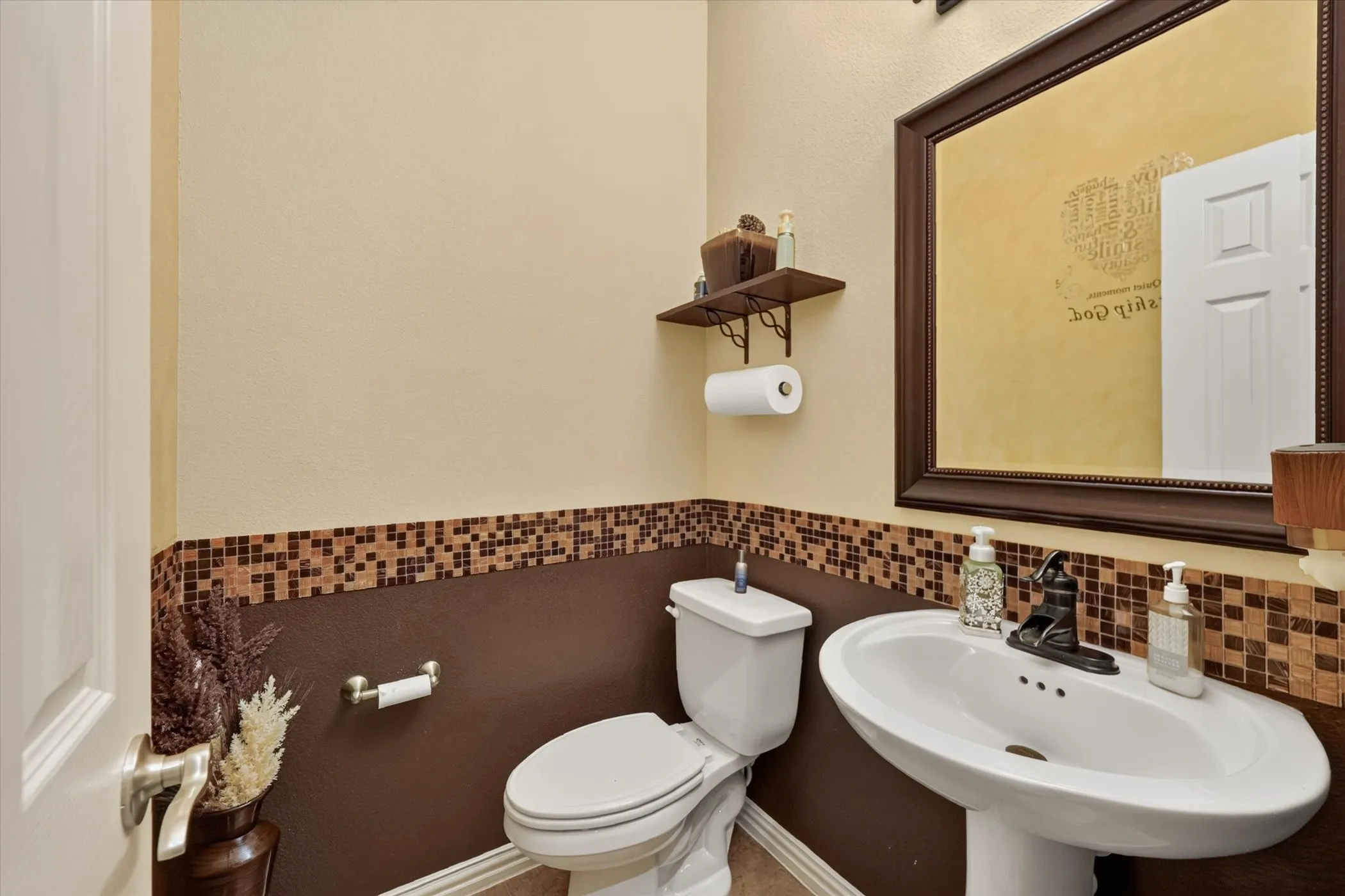 Pedestal sink with dark-toned faucet, wall-mounted mirror, and tile wainscoting