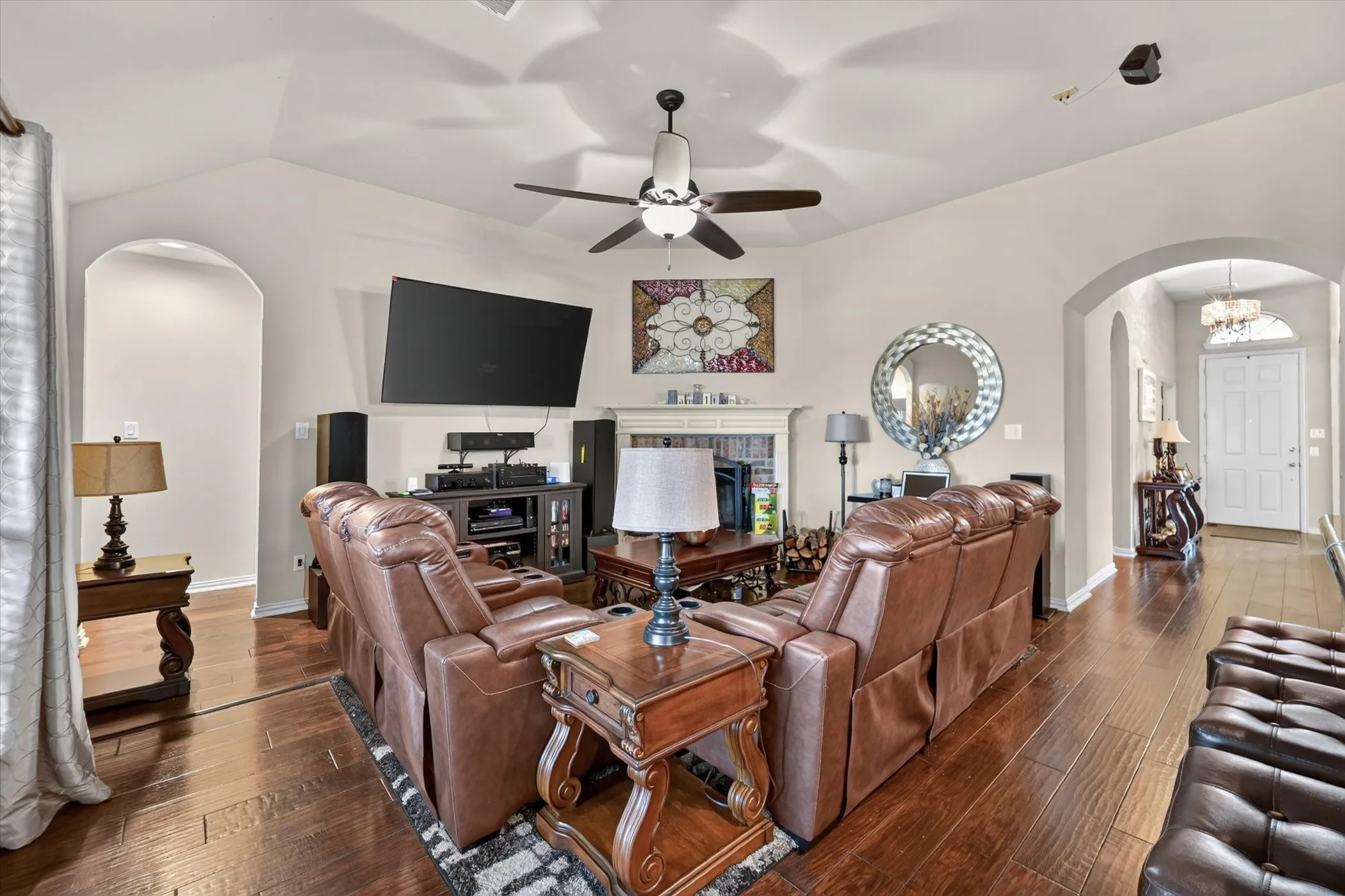 Vaulted ceiling with a ceiling fan, arched doorways, fireplace with mantel, and wood-finish​​‌​​​​‌​​‌‌​‌‌​​​‌‌​‌​‌​‌​​​‌​​ flooring