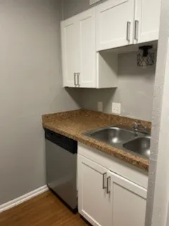 White shaker-style cabinetry, stainless steel double basin sink, speckled countertop, wood-finish flooring, and a stainless steel dishwasher