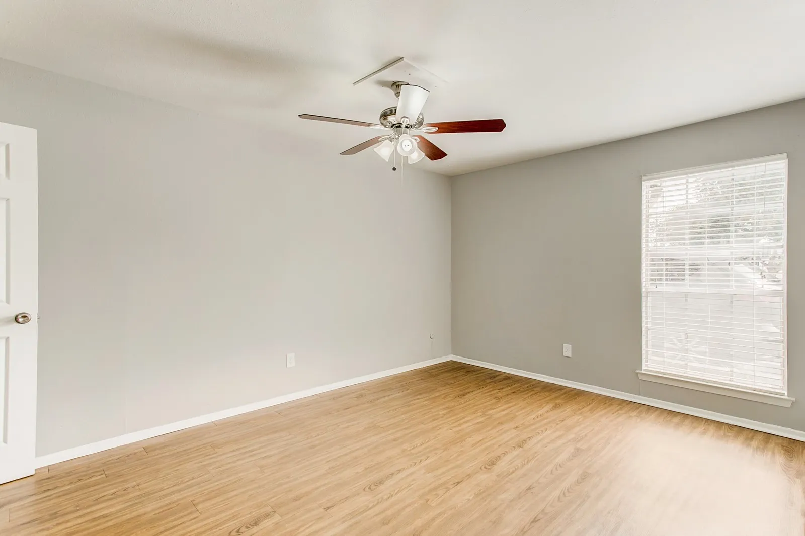 Wood-finish flooring, light gray wall paint, a window with blinds, and a ceiling fan with integrated lighting