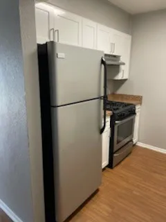 Stainless steel refrigerator, stainless steel range, white cabinetry, wood-finish flooring, and light-toned countertops