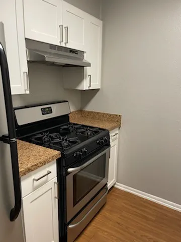 Stainless steel range with oven, white upper and lower cabinetry, wood-finish flooring, and light-toned countertops