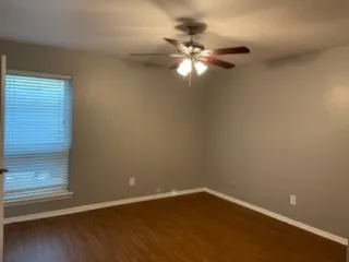 Wood-finish flooring, neutral wall tones, window with horizontal blinds, and a ceiling fan with integrated lighting