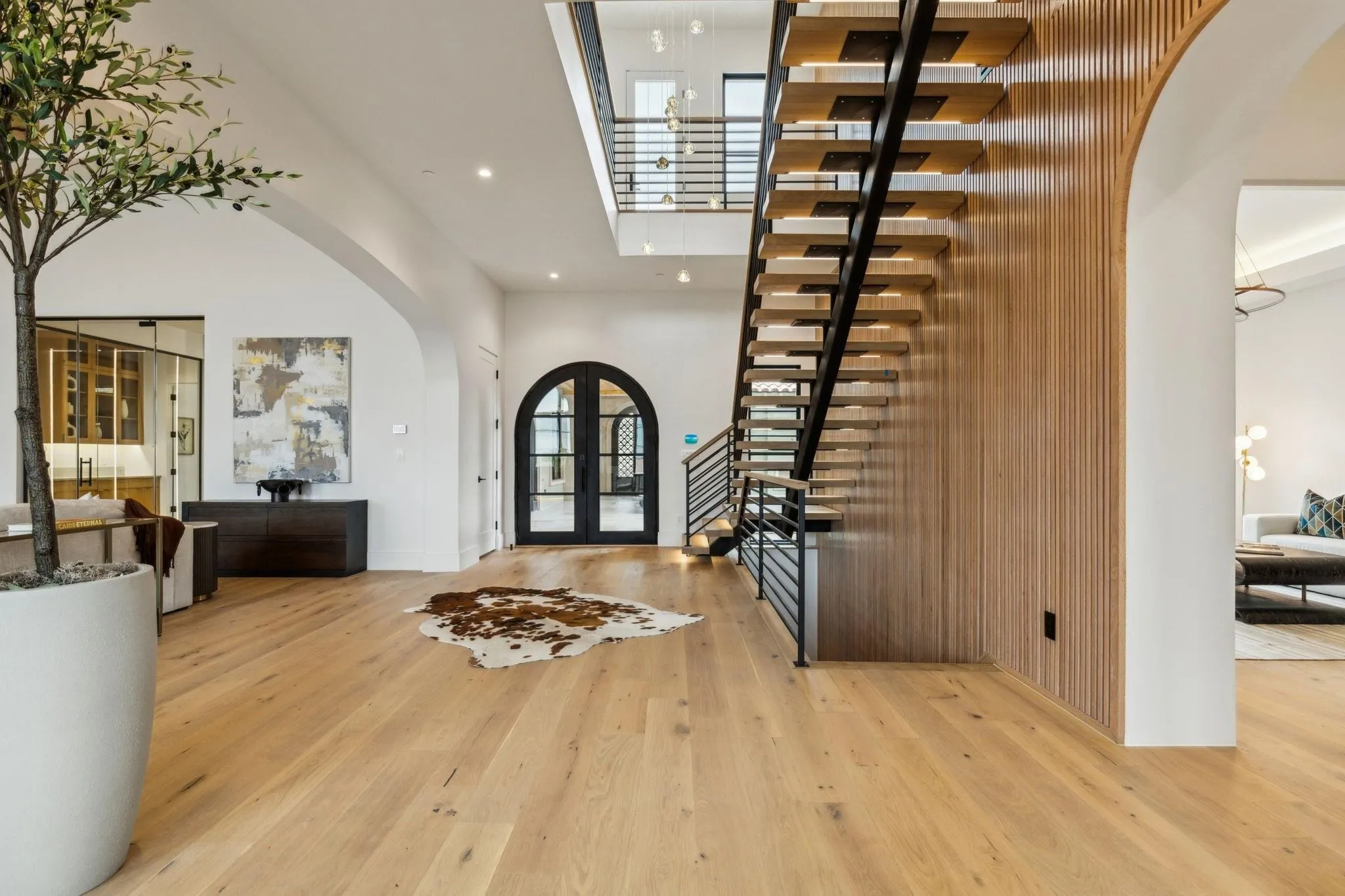 Foyer featuring arched walkways, a high ceiling, light wood-style flooring, recessed lighting, and stairs