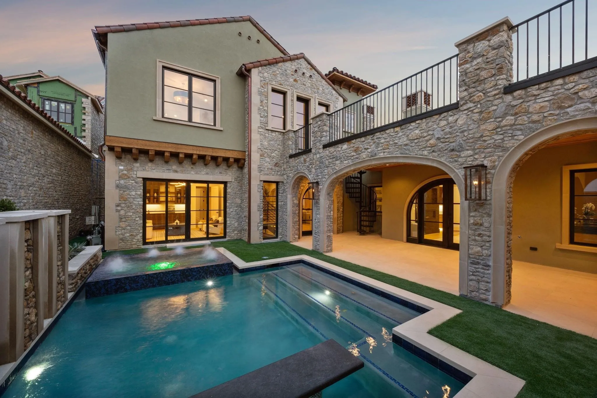 Courtyard at dusk featuring a balcony, stone siding, and a patio