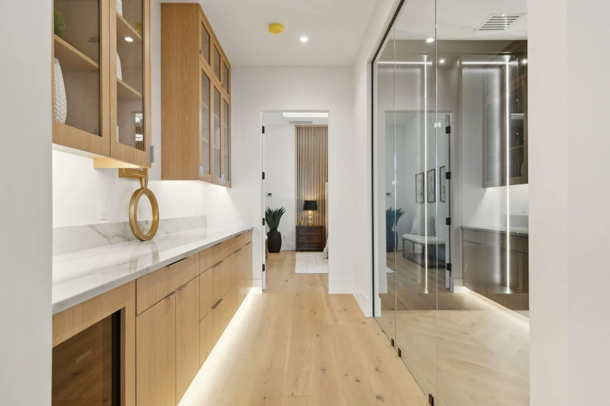 Large coffee bar just outside owners suite with beverage refrigerator, under cabinet lighting, stone countertops, and white oak flooring.