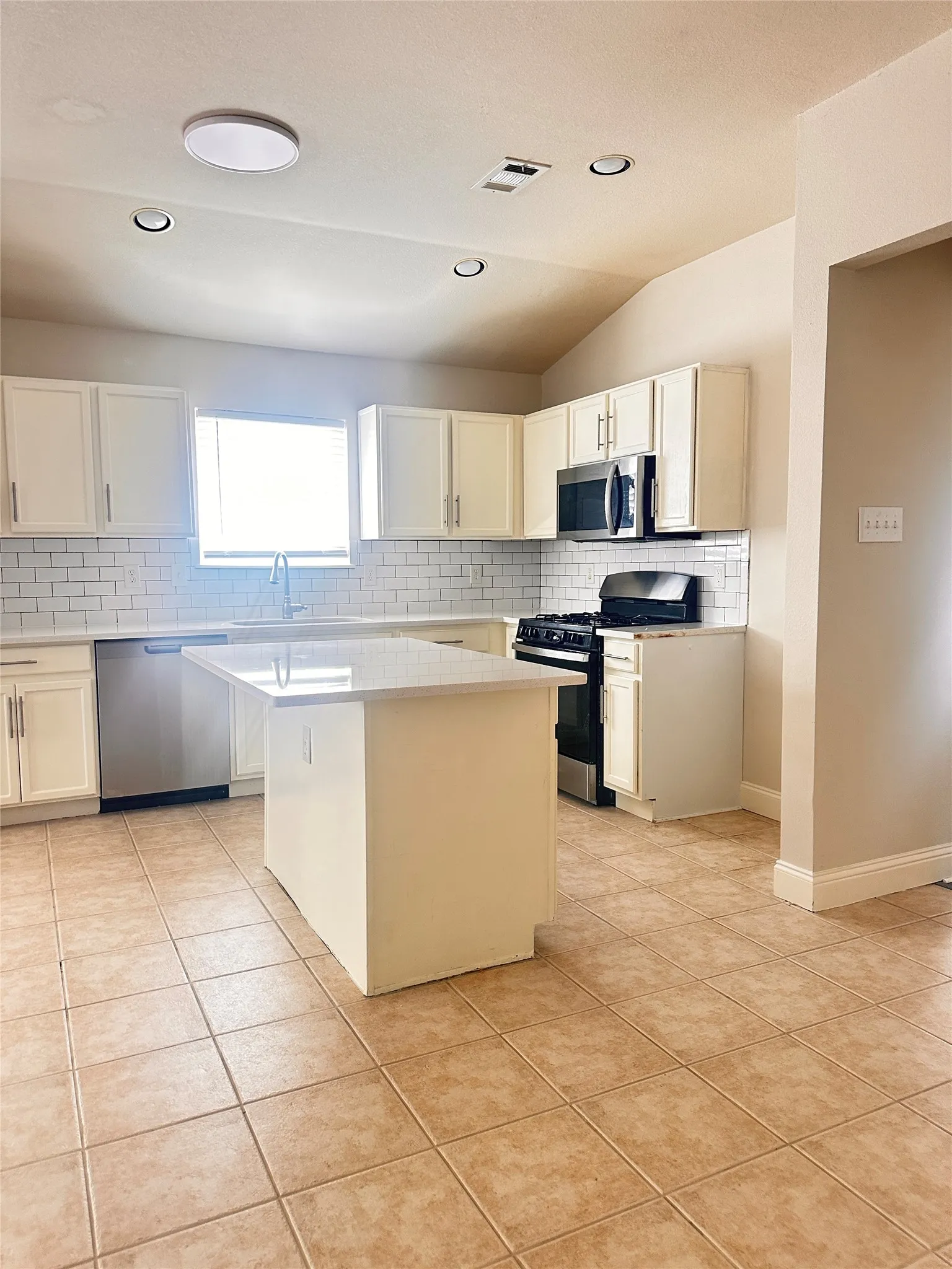Kitchen with backsplash, stainless steel appliances, a kitchen island, light tile patterned flooring, and white cabinetry