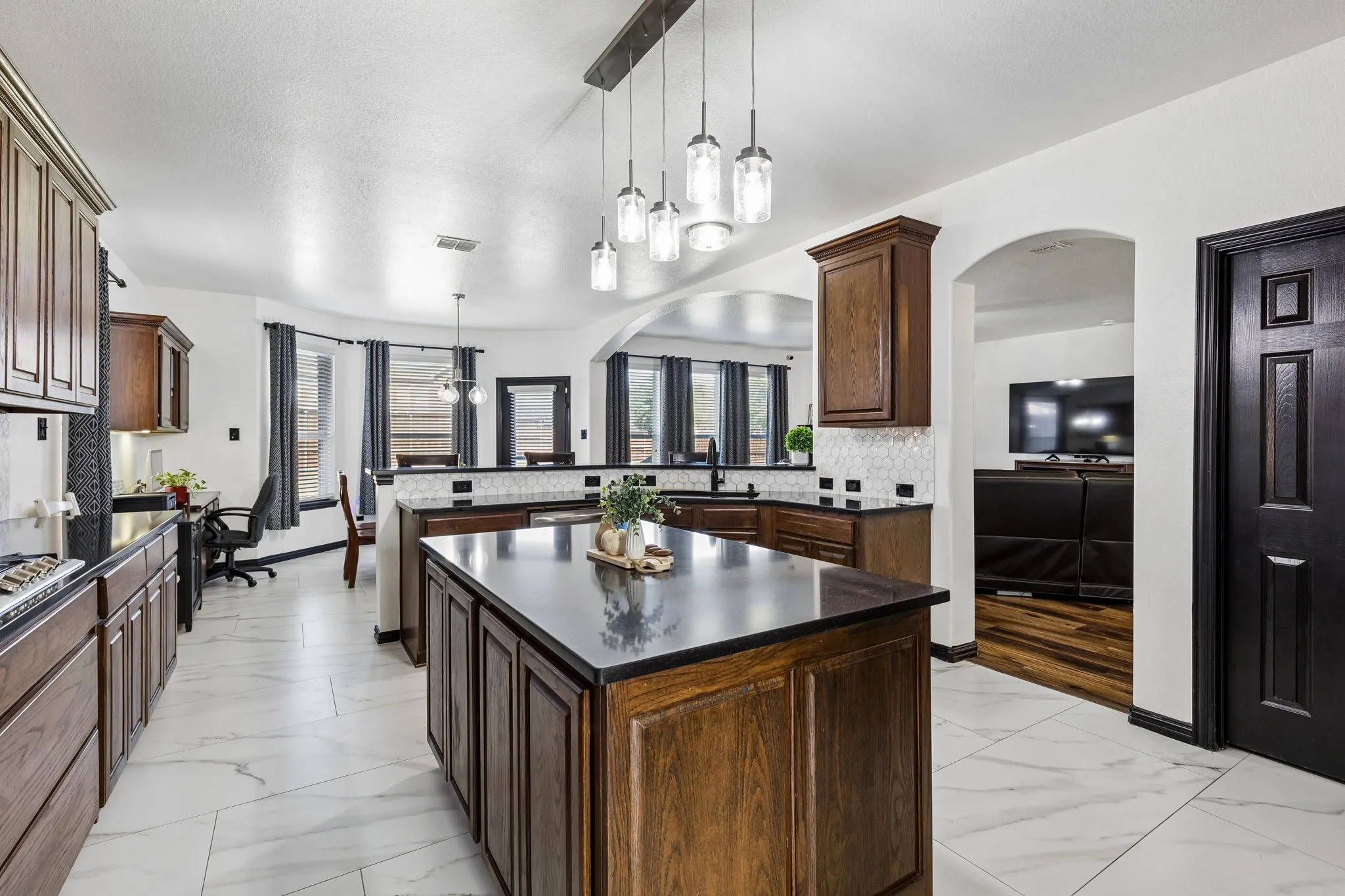 A Kitchen That Brings Everyone Together – The beautifully updated kitchen features a large center island, upgraded custom wood-grain cabinetry, stylish pendant lighting, and generous countertop space, with open sightlines to the adjoining living and dining areas.