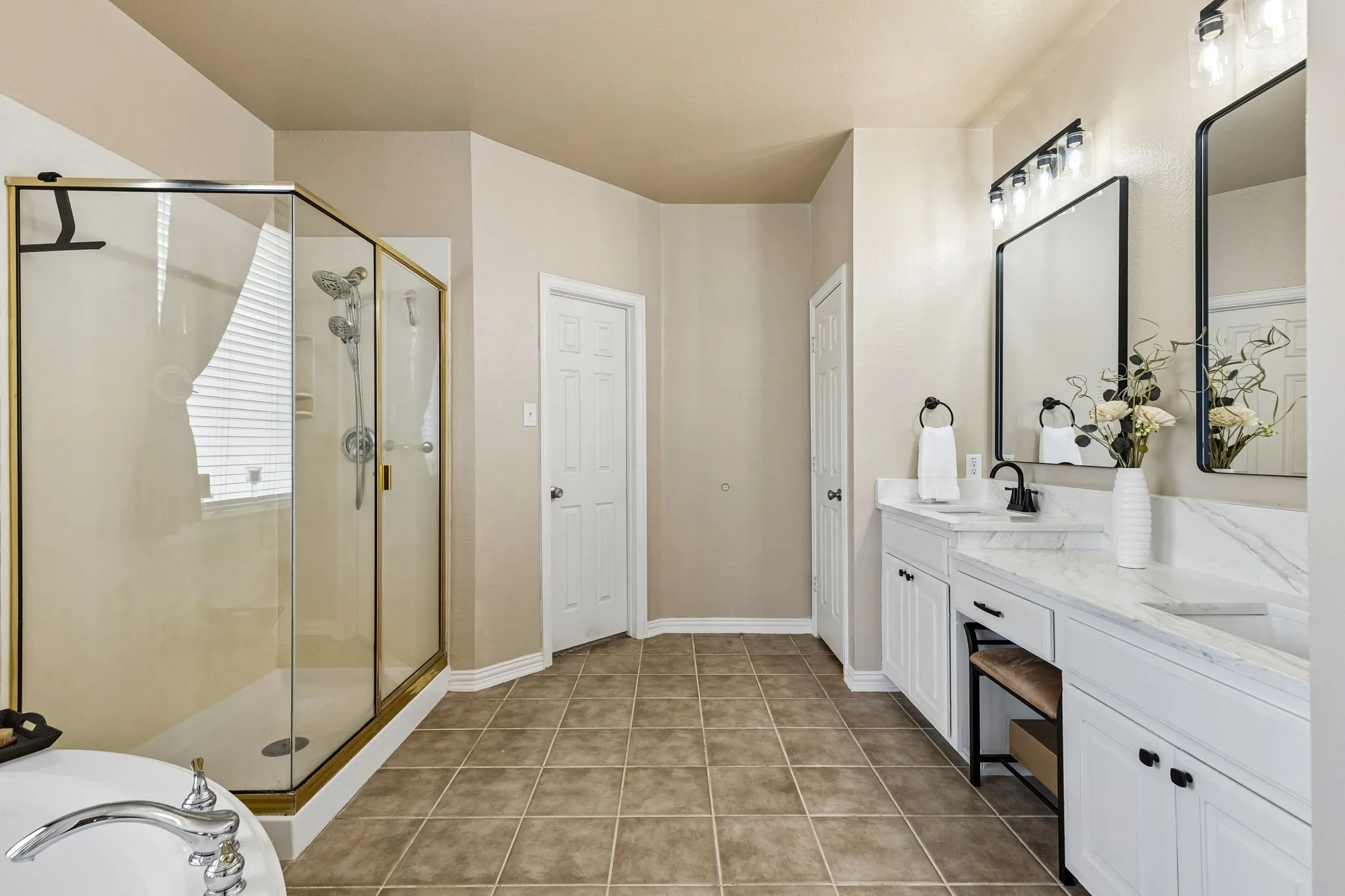 Spacious Primary Bath with Updated Finishes – The generously sized primary bathroom features a separate walk-in shower, updated quartz-topped vanities, framed mirrors, modern lighting, and tile flooring, with convenient access to the linen closet and walk-in closet.