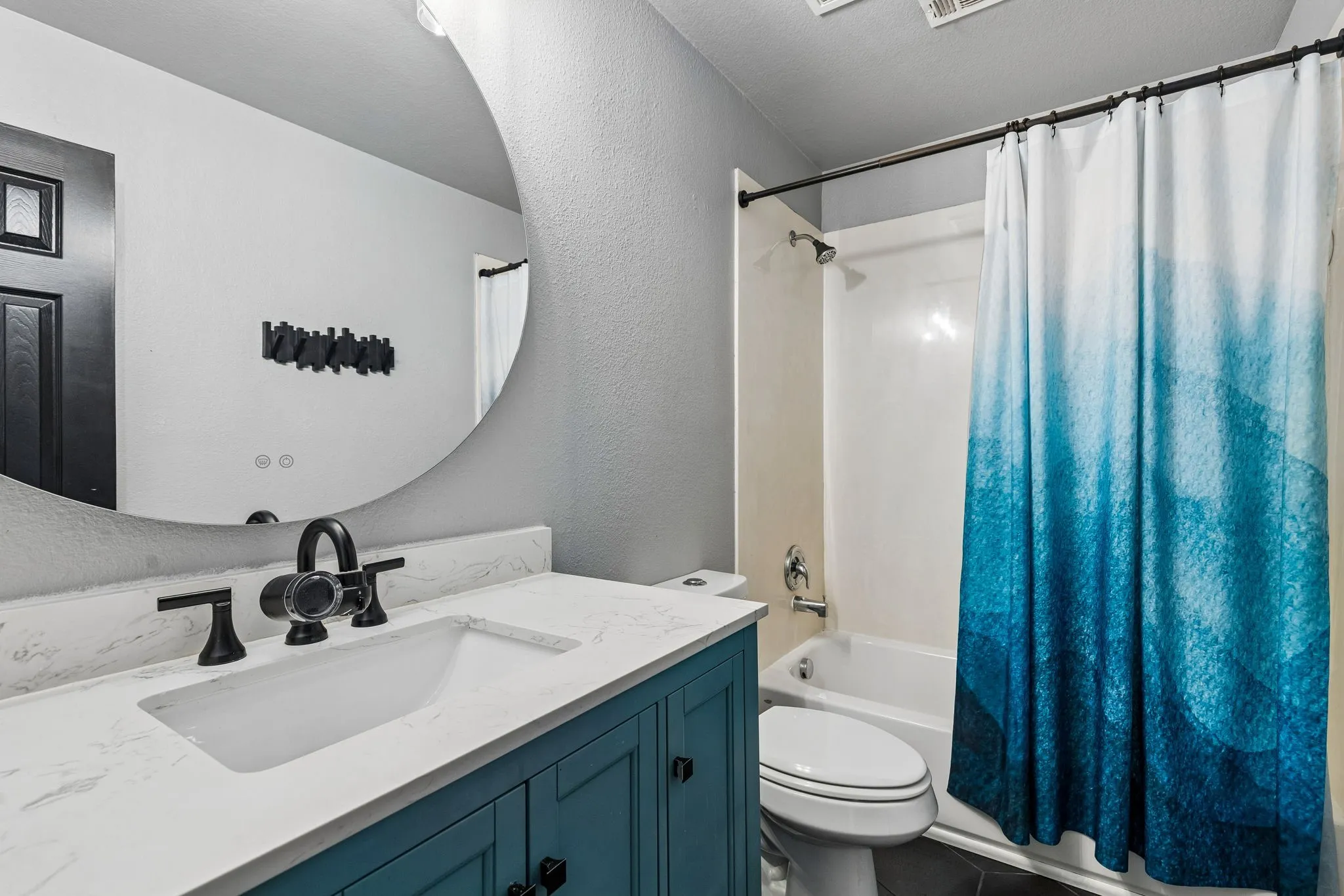 Updated Upstairs Bath – A stylish blue vanity cabinet topped with quartz features an undermount sink and matte black fixtures. Updated flooring, a contemporary mirror, and a tub-shower combination complete this refreshed full bathroom.