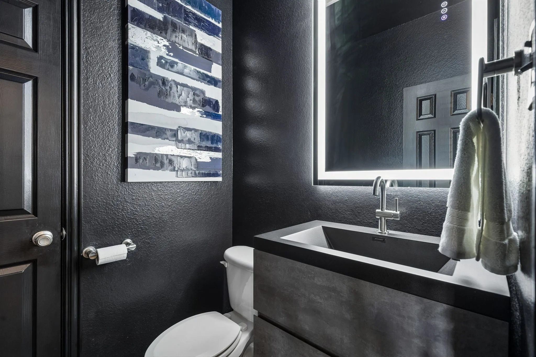A Powder Bath with Personality – This striking half bath makes a bold statement with black walls, coordinating trim, and a contemporary floating vanity featuring an integrated rectangular sink. An illuminated mirror and modern fixtures complete the updated look.