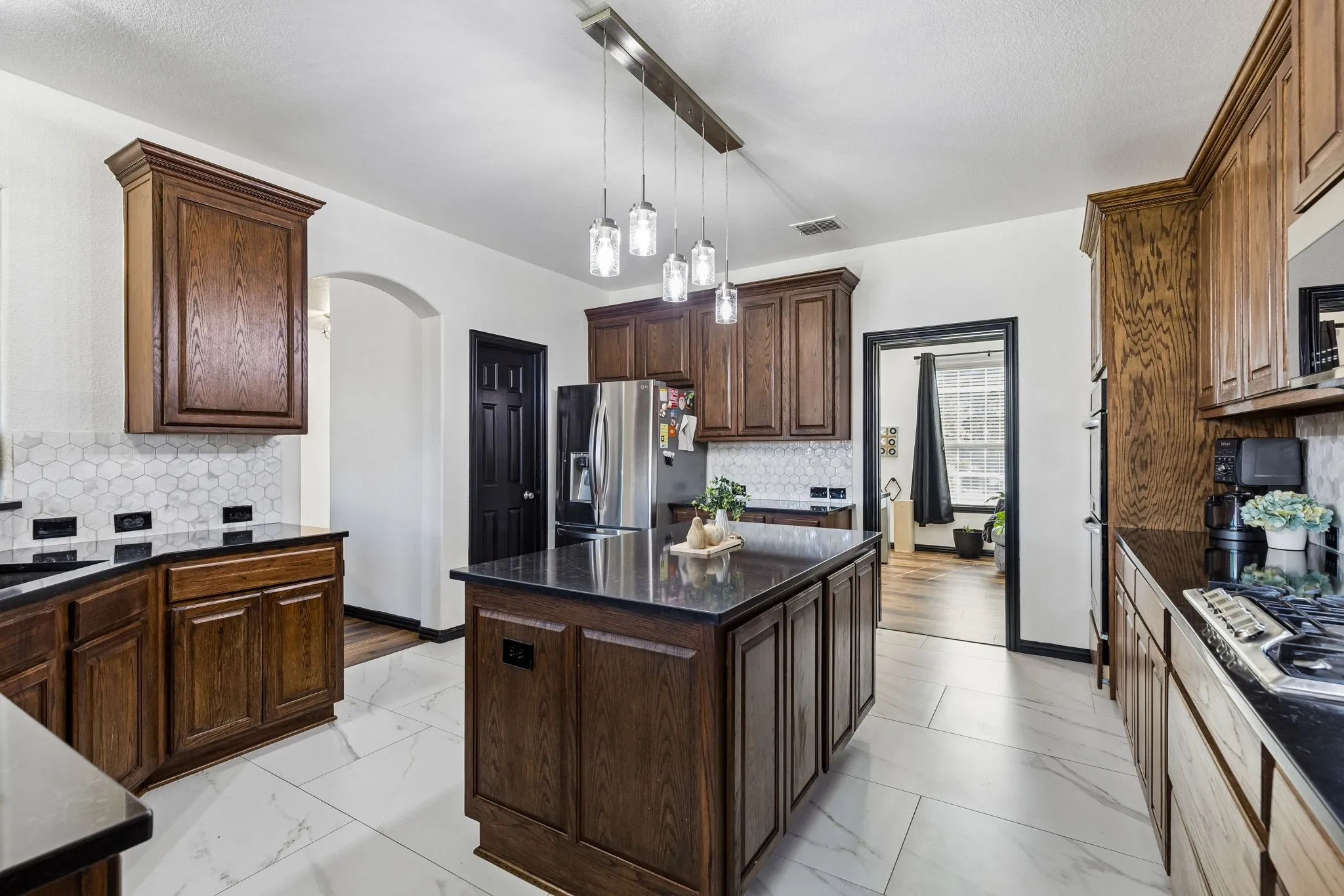Style and Function in Every Detail – Richly finished cabinetry, sleek dark countertops, and a designer hexagon tile backsplash give this kitchen a distinctive look, while the spacious island provides an ideal surface for meal preparation and serving.