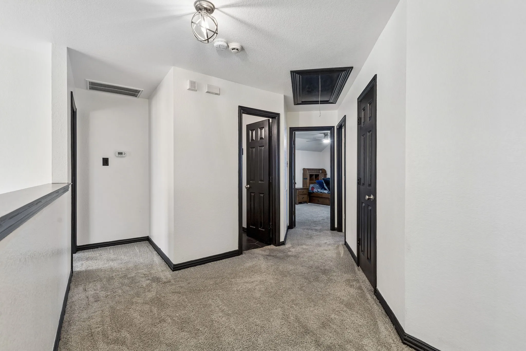 Convenient Upstairs Bedroom Layout – A spacious second-floor hallway connects the secondary bedrooms and bathroom, featuring carpeting, updated lighting, and contrasting black doors and trim that carry the home's distinctive style throughout.