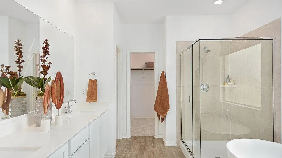 Double vanity with integrated sinks, wood-finish flooring, recessed lighting, walk-in shower with glass enclosure, and built-in shelving