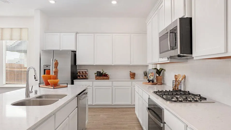 Kitchen featuring white cabinetry, light-toned countertops, stainless steel appliances, a double basin sink, and a built-in microwave