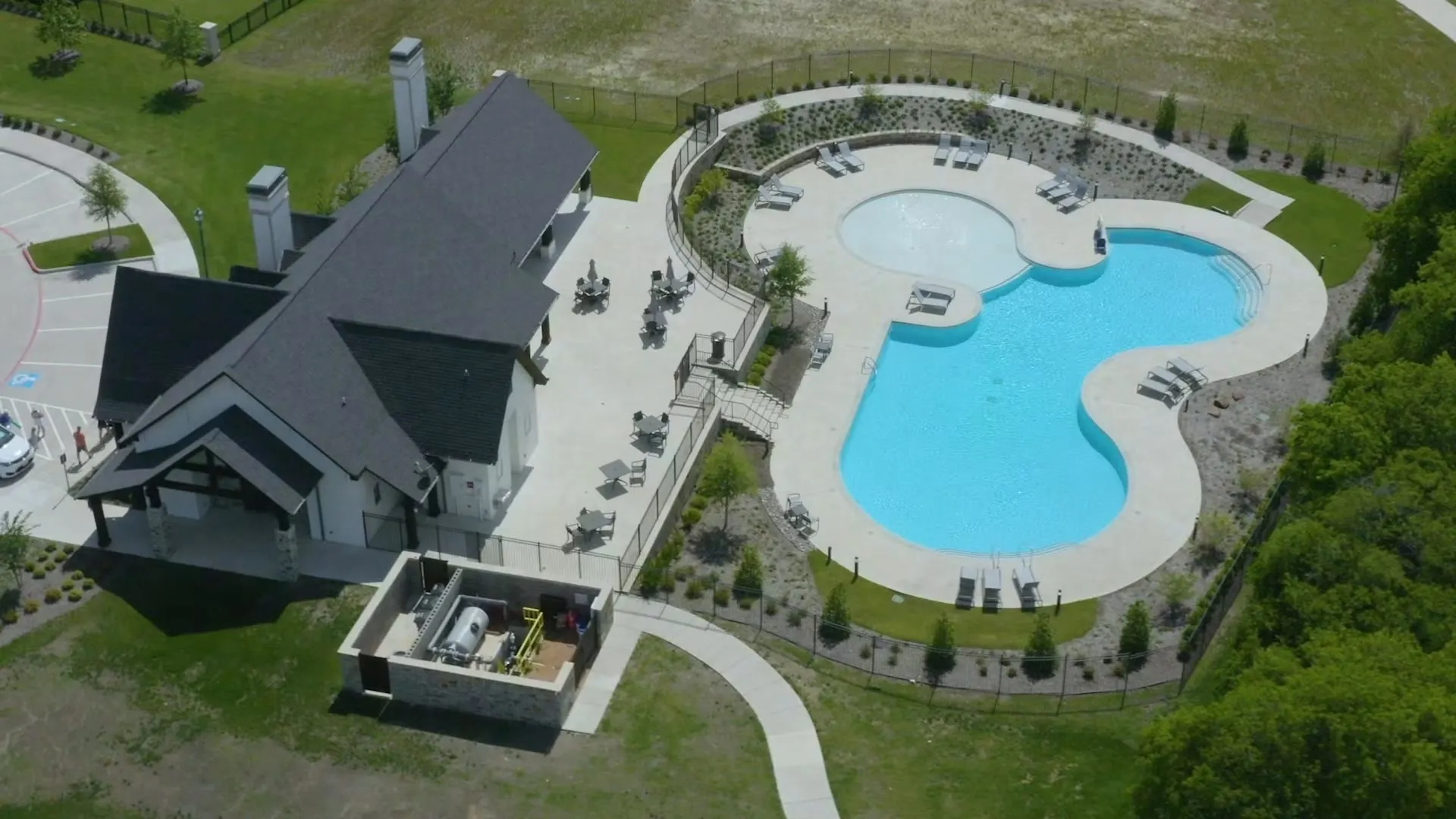 Clubhouse featuring a covered patio, adjacent swimming pool with integrated spa, and expansive paved deck area