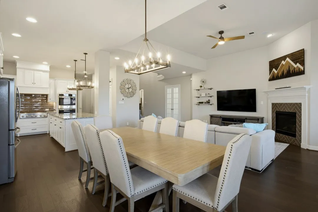 Open-concept living space featuring wood-finish flooring, a kitchen with white cabinetry and an island, a fireplace with a herringbone tile surround, and recessed lighting