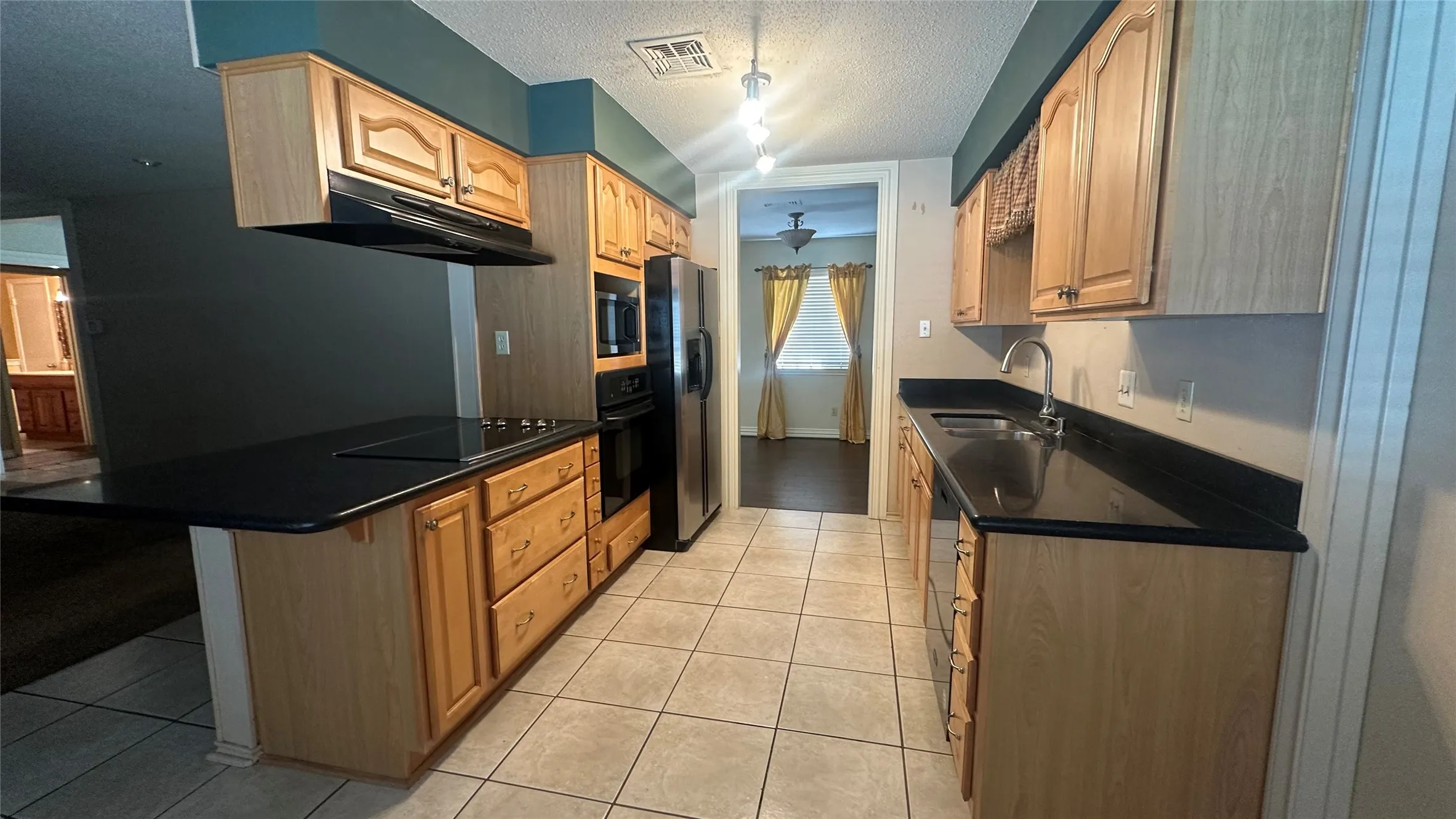Kitchen with wood cabinetry, black countertops, and a built-in cooktop island.  Breakfast area off kitchen - entry into the formal dining for serving dinner.