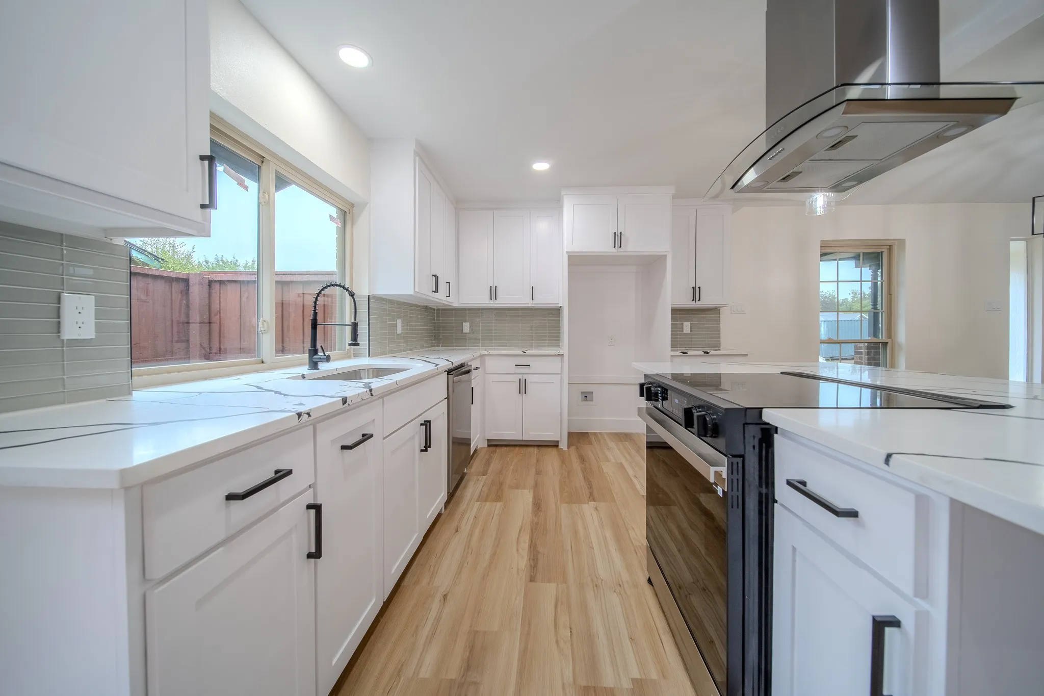 Modern kitchen featuring white cabinetry, light wood-finish flooring, white countertops with veining, a stainless steel range hood, and a black range