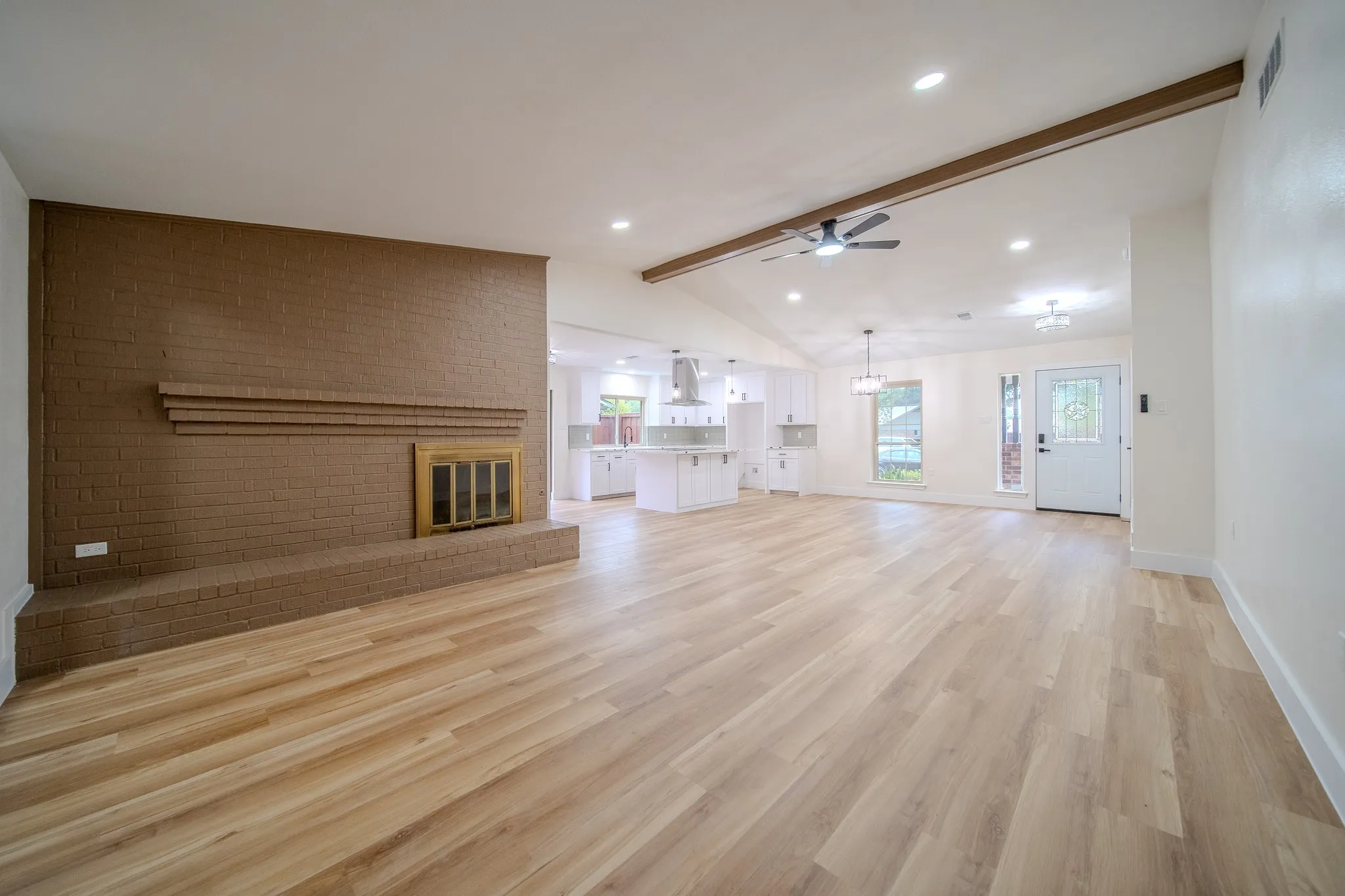 Expansive main living area featuring wood-finish flooring, a brick fireplace, and vaulted ceilings with exposed beams