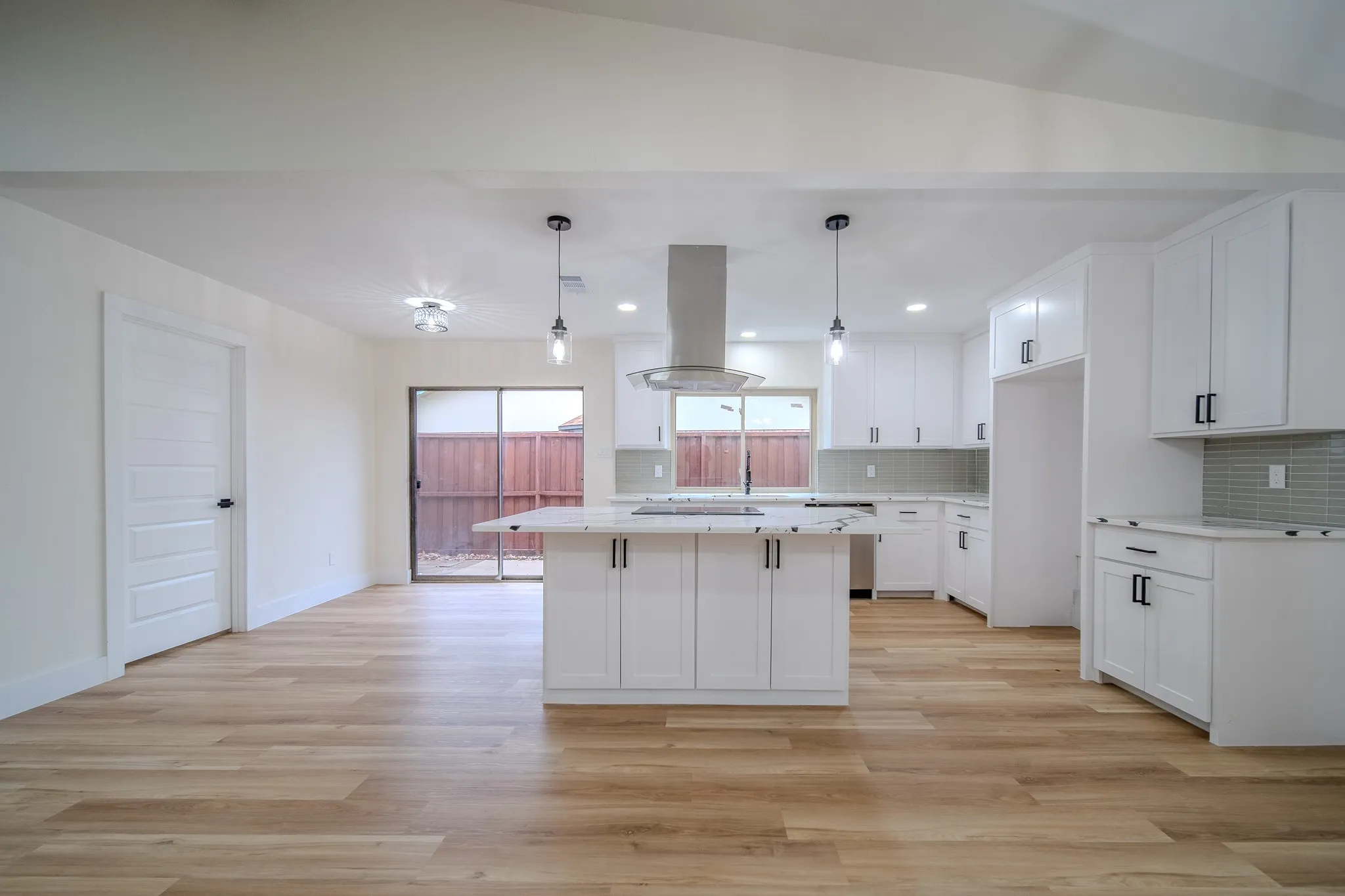 Vaulted ceilings with recessed lighting, wood-finish flooring, white shaker cabinetry with black hardware, a kitchen island with a cooktop, and a tile backsplash