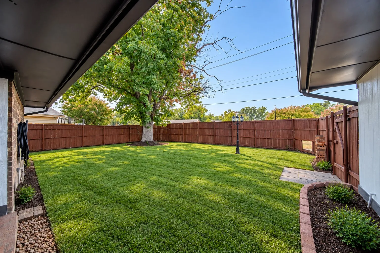 Expansive backyard featuring a lush lawn, privacy fencing, mature trees, and a paved patio area(staged with grass)