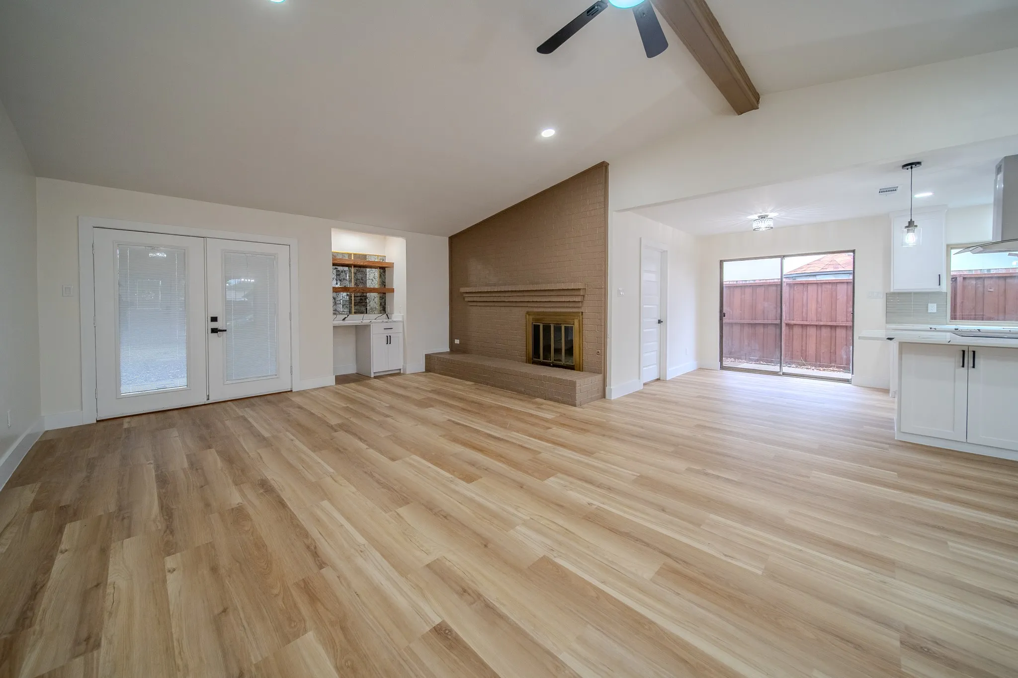 Vaulted ceiling with an exposed beam, light wood-finish flooring, brick fireplace, and sliding glass door