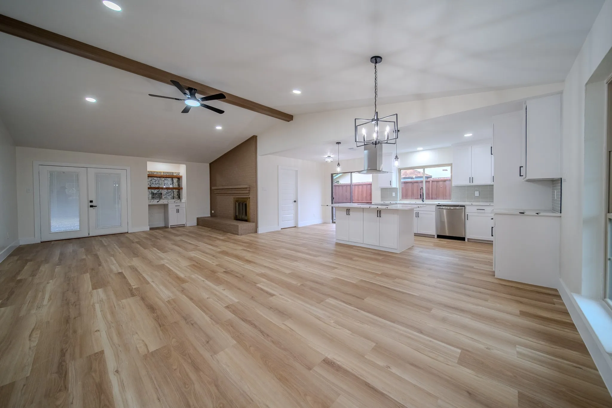 Vaulted ceilings with exposed beam, wood-finish flooring, white shaker cabinetry, stainless steel appliances, and a built-in fireplace