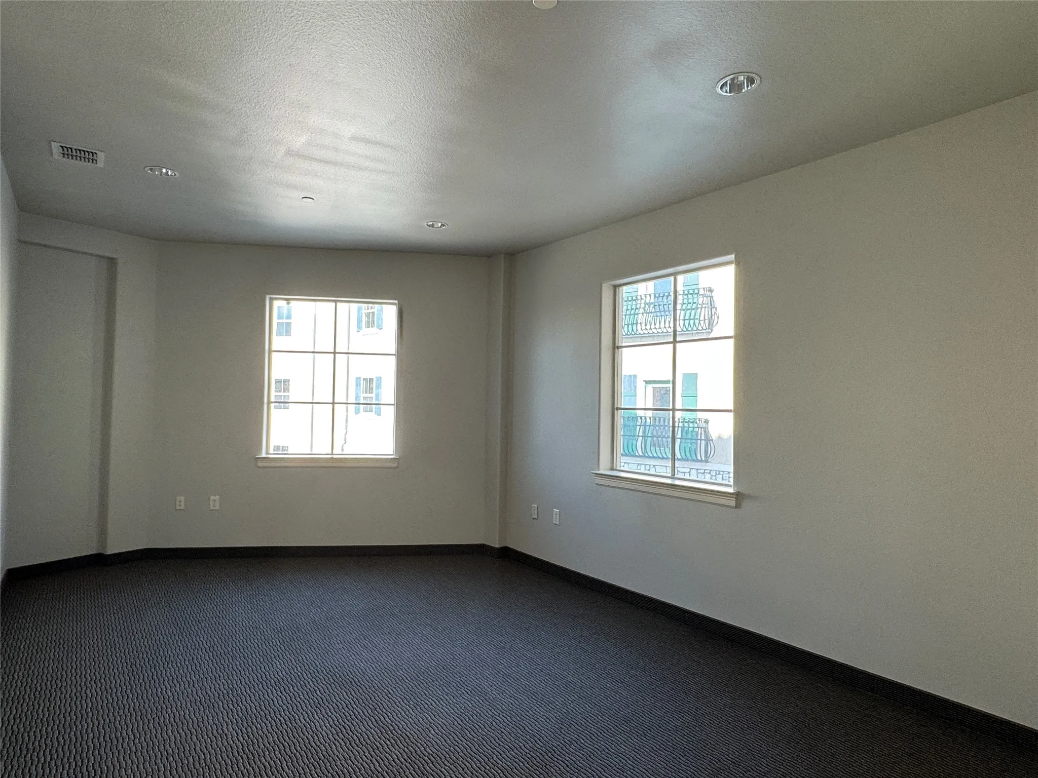 Spacious room featuring patterned carpet, multiple recessed ceiling lights, and two windows with white trim