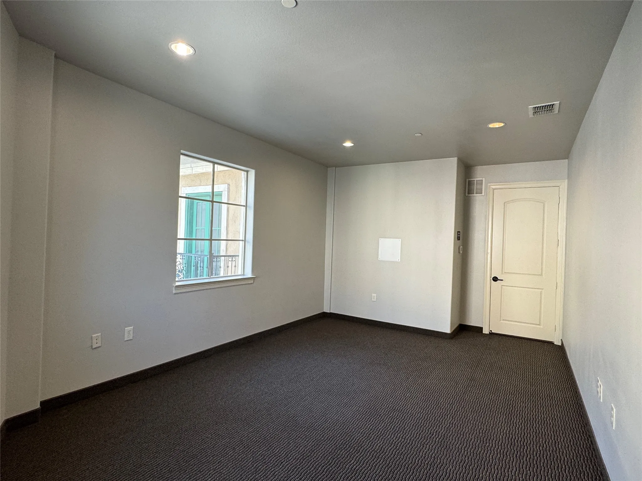 Recessed lighting, window with grid panes, neutral wall paint, dark patterned carpet, and paneled interior door