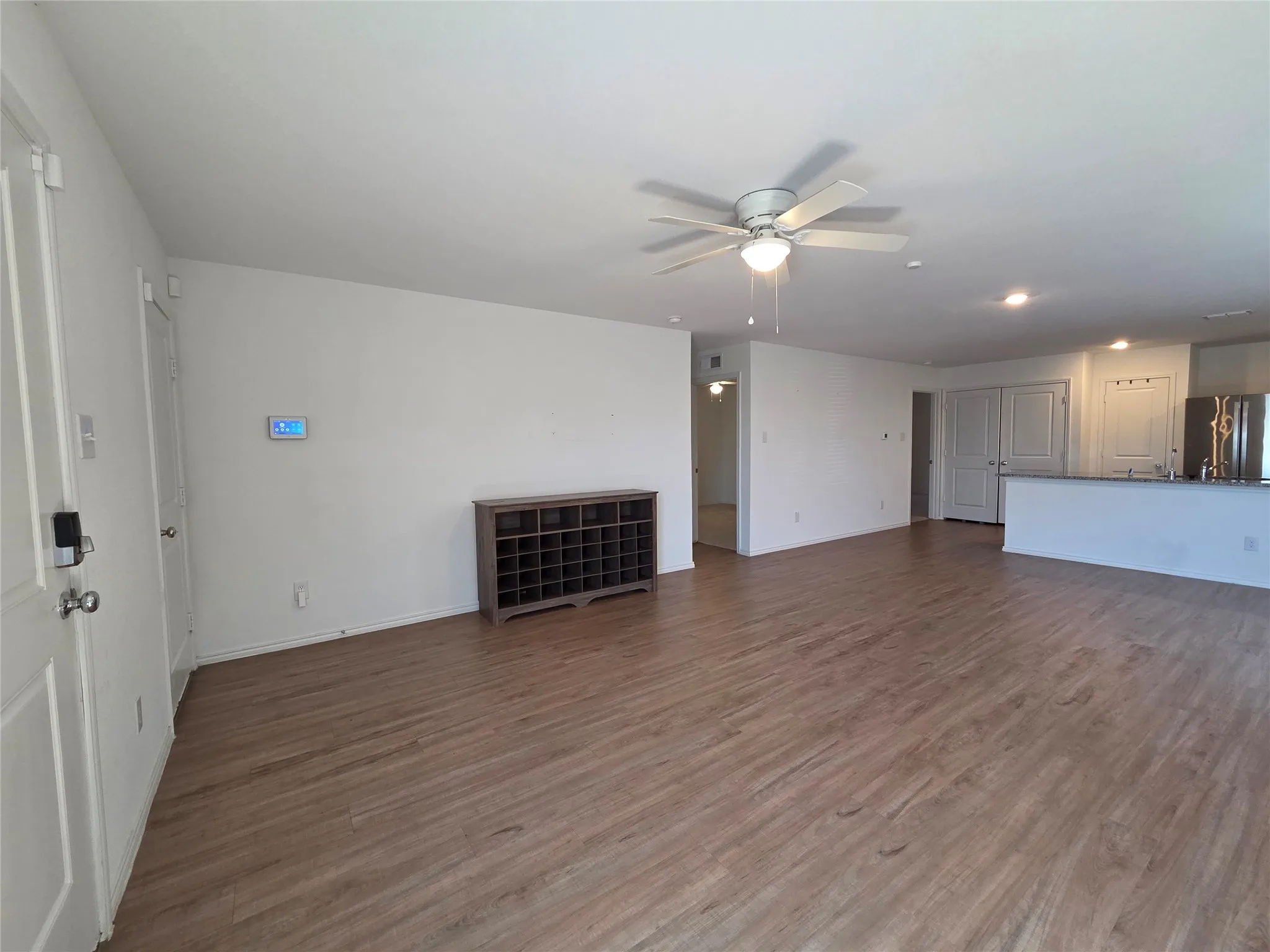 Spacious room featuring wood-finish flooring, white walls, and a ceiling fan with integrated lighting