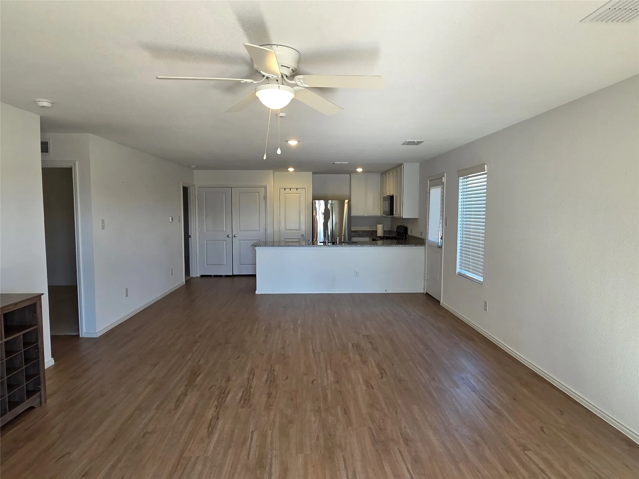 Open-concept layout featuring wood-finish flooring, white walls, and a ceiling fan with integrated lighting
