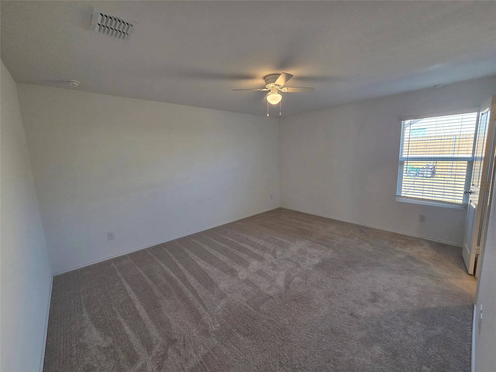 Carpeted flooring, white painted walls, ceiling fan with integrated lighting, window with horizontal blinds, and a white interior door