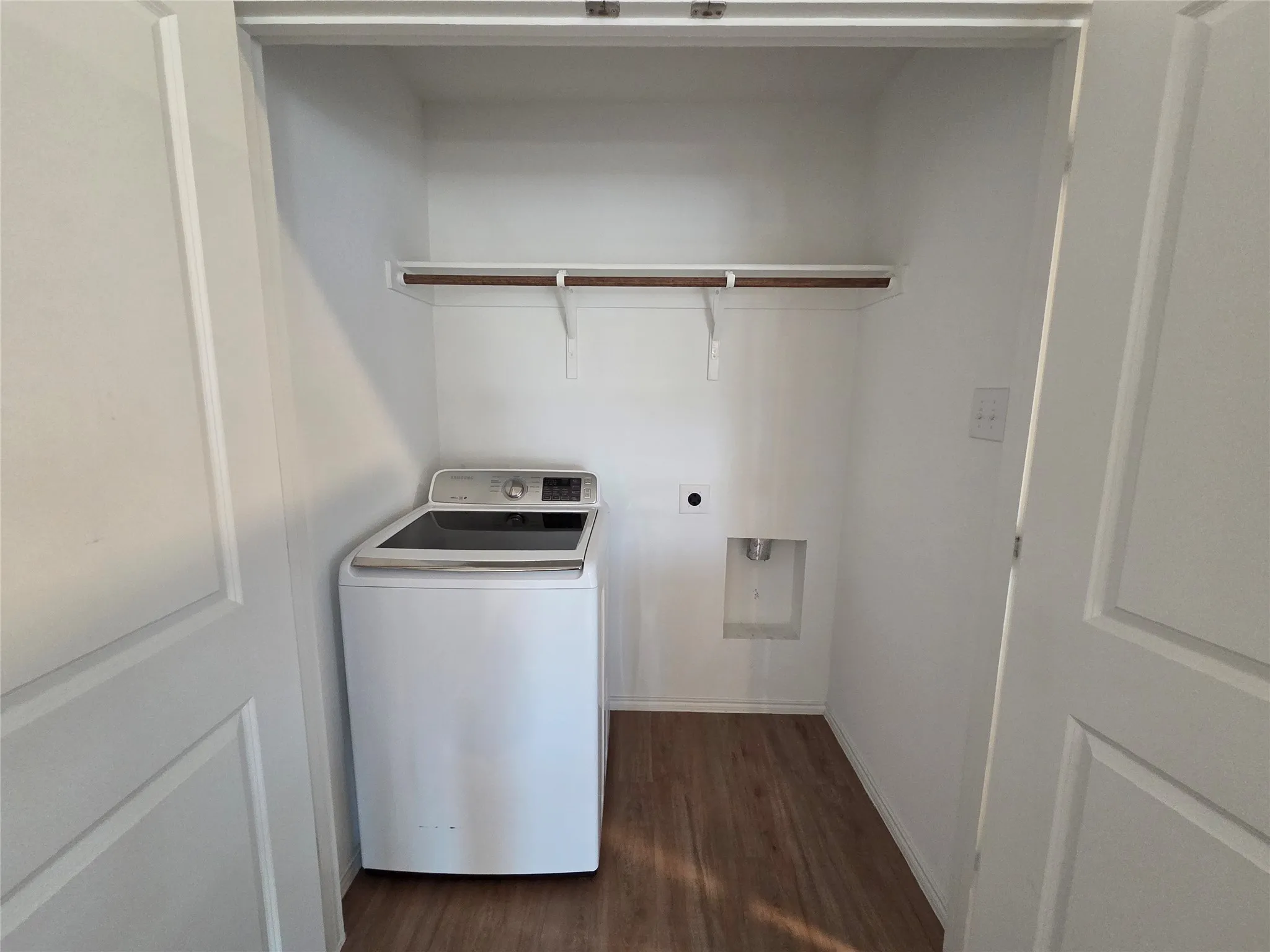 Dedicated laundry closet featuring a wood-finish flooring, built-in shelving, and a wall-mounted outlet