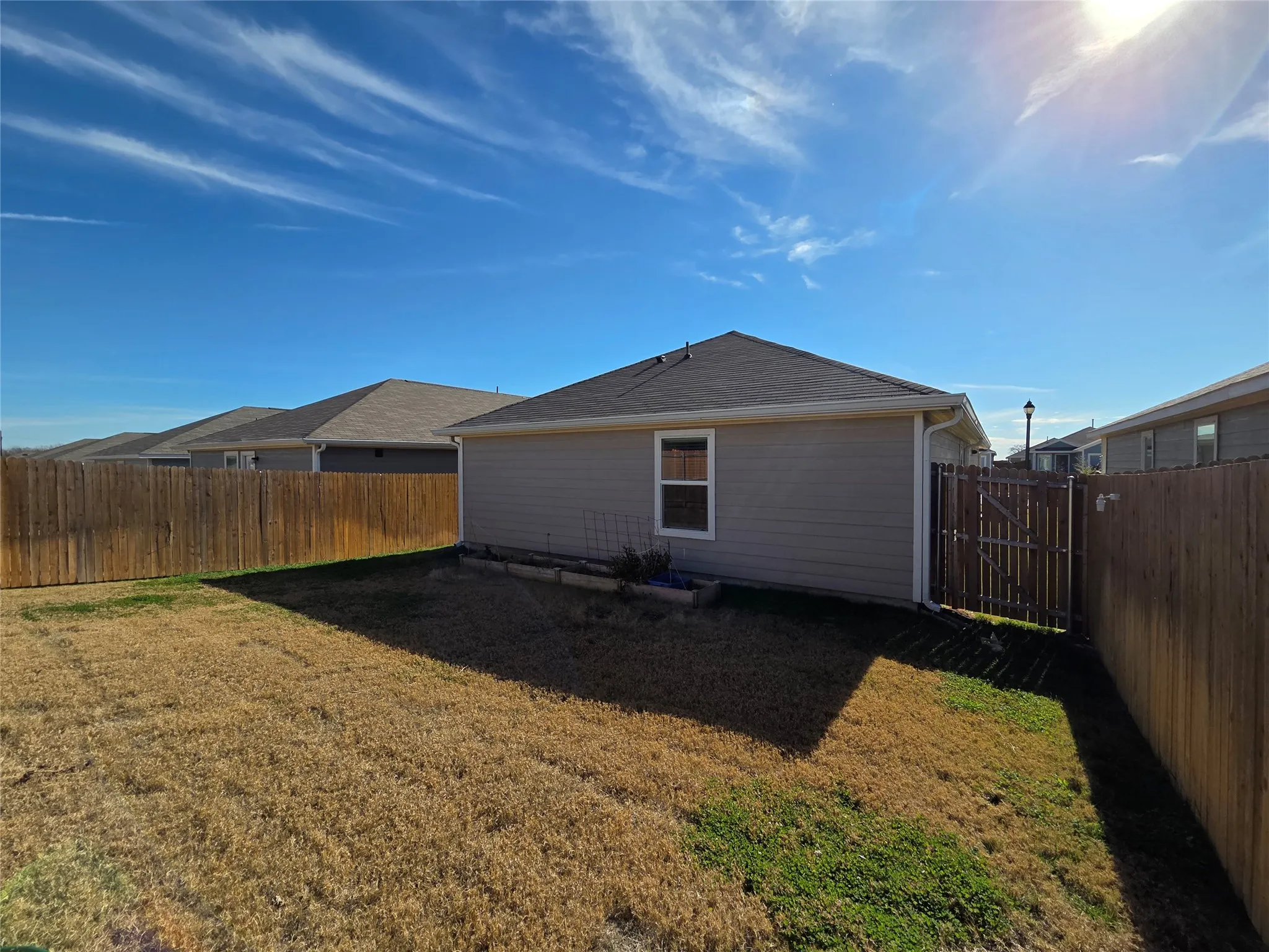 Expansive backyard featuring a wood privacy fence, a side gate, and a single window on the exterior wall