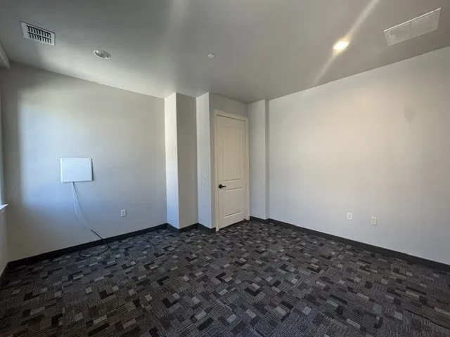 Recessed ceiling lighting, patterned carpet flooring, white interior door, and light-colored walls