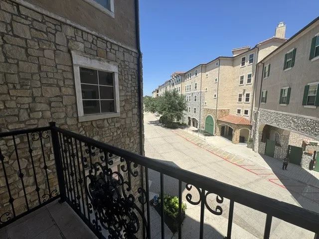 Wrought iron balcony railing with decorative scrollwork, stone exterior accents, tiled balcony flooring, and multi-story building facade