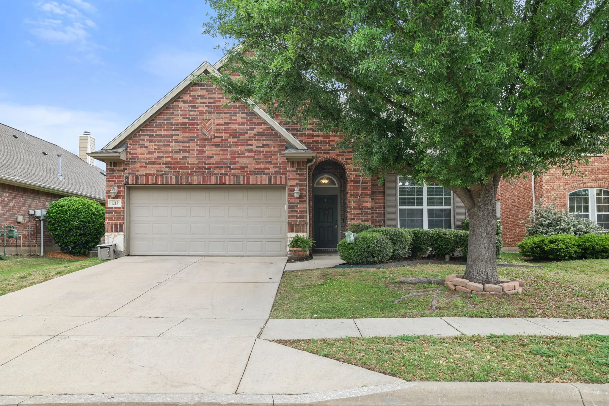 Brick exterior with gabled roofline, arched entry, mature front tree, and attached garage