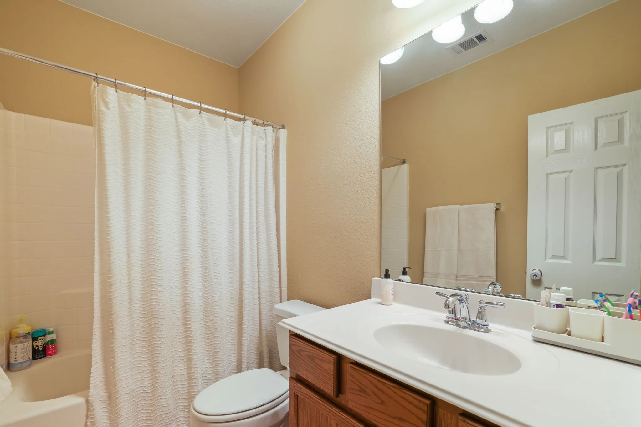 Bathroom with a white tub and shower surround, a white toilet, and a vanity with a white countertop and wood-finish cabinetry